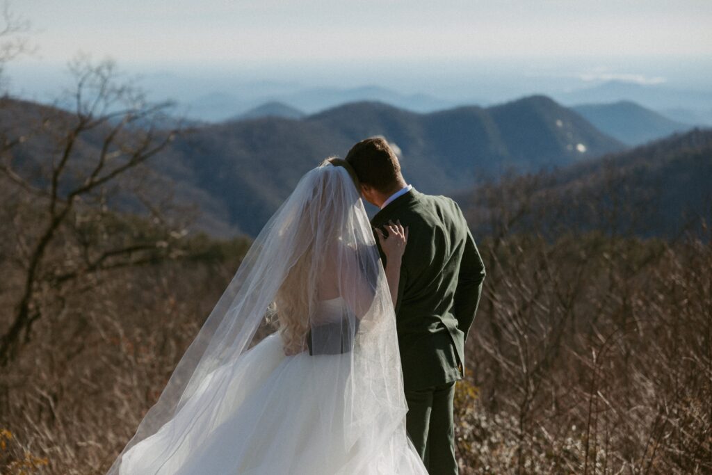 Man and woman in wedding attire looking at mountains at Sassafras Mountain in South Carolina.