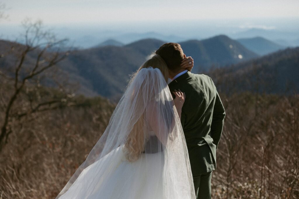 Man and woman in wedding attire looking out at the mountains.