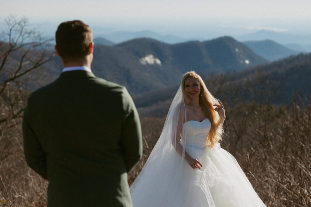 Man looking at woman in wedding dress with mountains behind her.