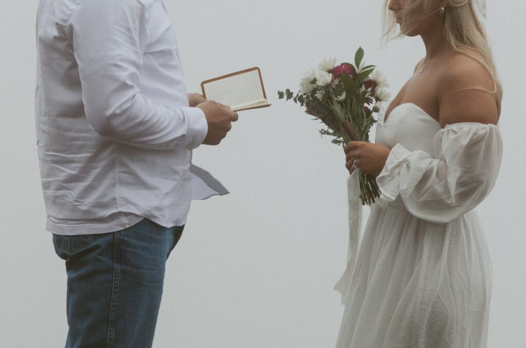 Man and woman holding vow books while in wedding attire during elopement.