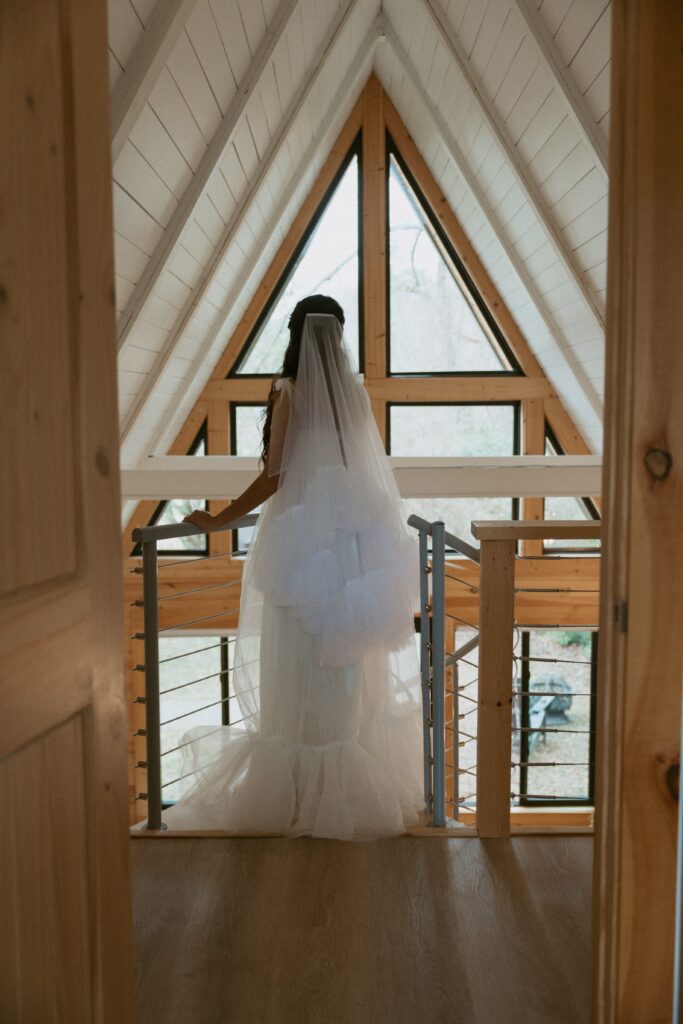 Woman standing at top of a-fram cabin stairs in a wedding dress. 