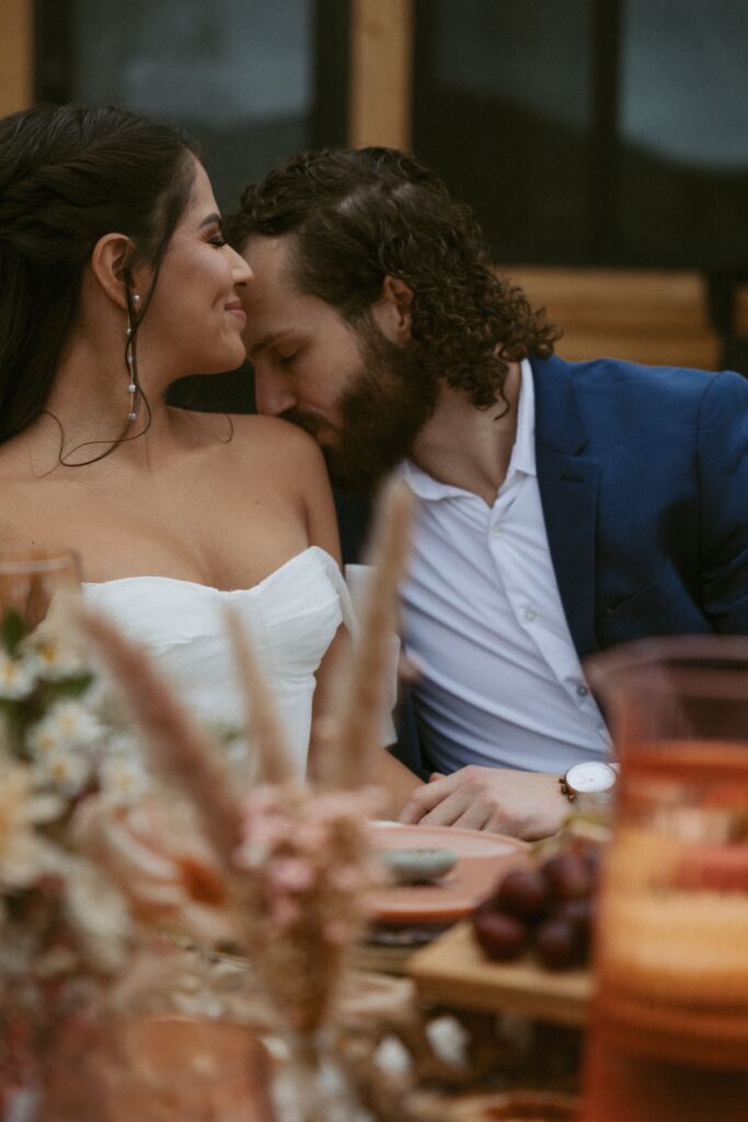 Man kissing woman on shoulder during picnic at wedding reception.