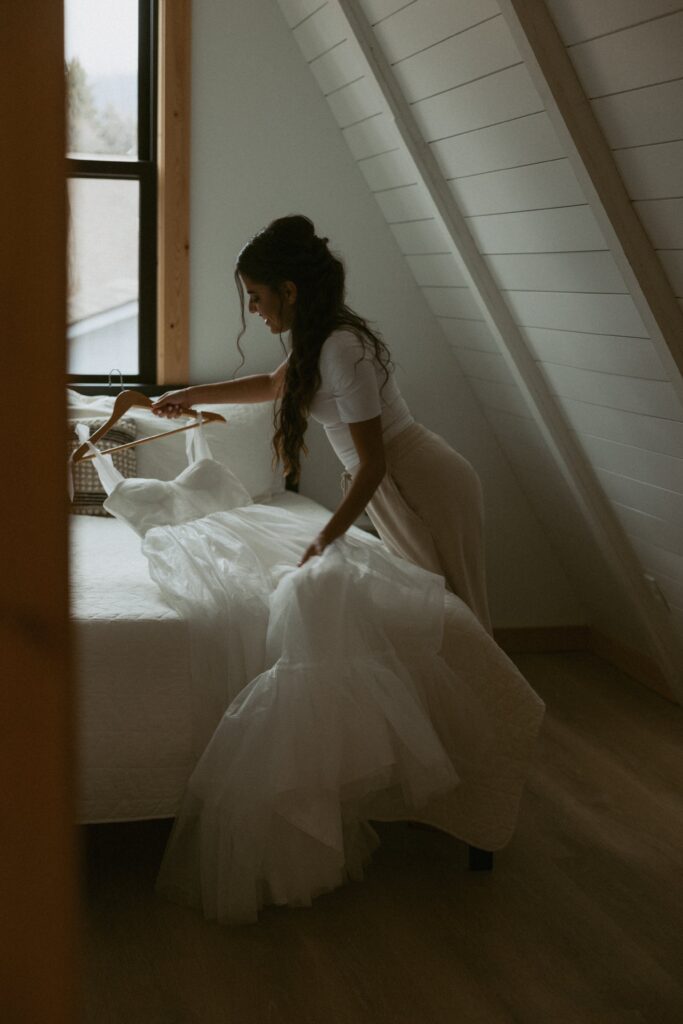 Woman picking wedding dress up off of a bed.