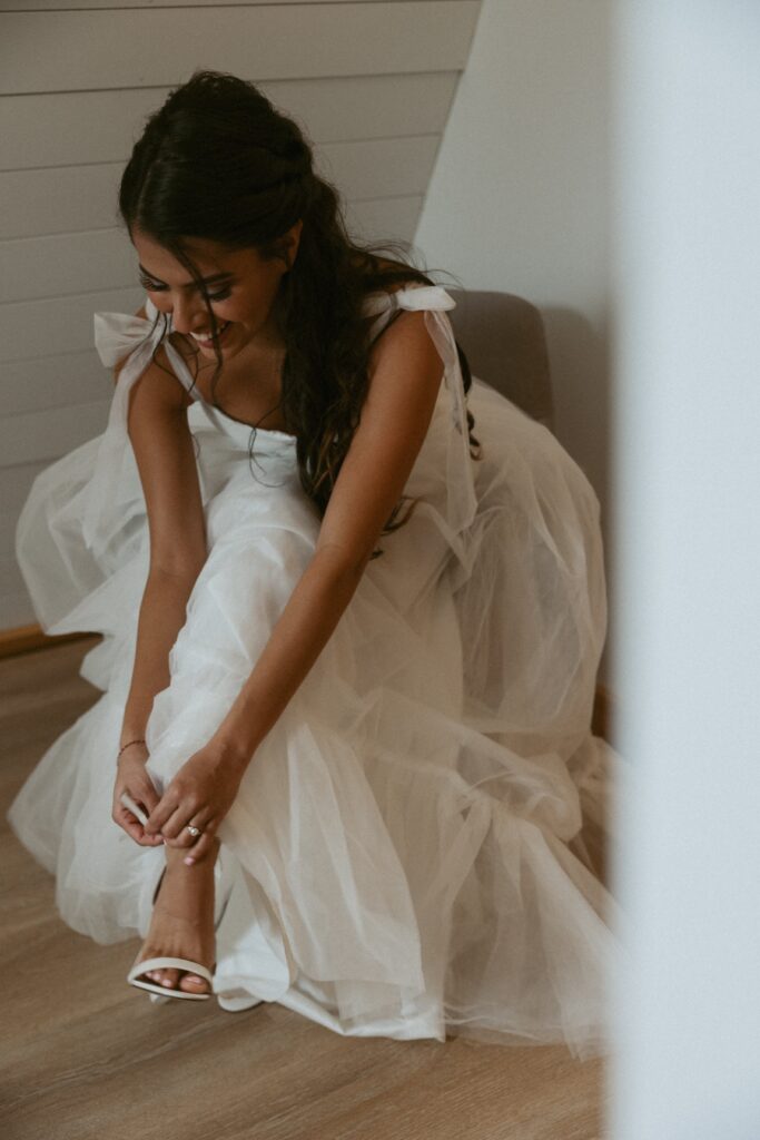 Woman in a wedding dress sitting and putting shoes on. 