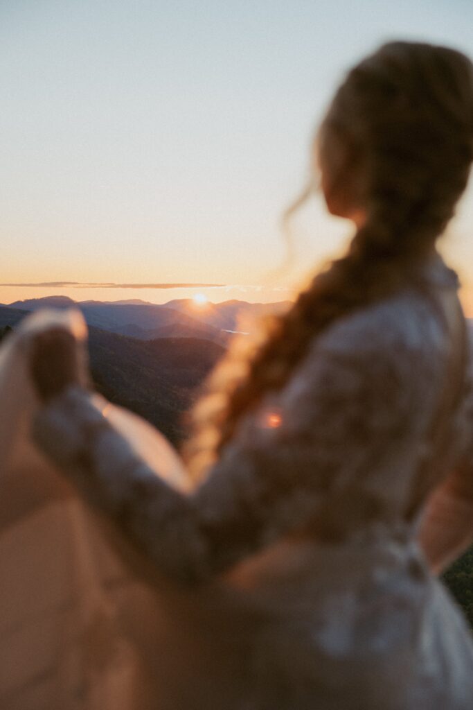 Woman in wedding dress looking at sunrise over the mountains.