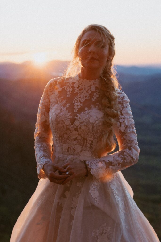 Woman in wedding dress playing with engagement ring at sunrise in front of the mountains.