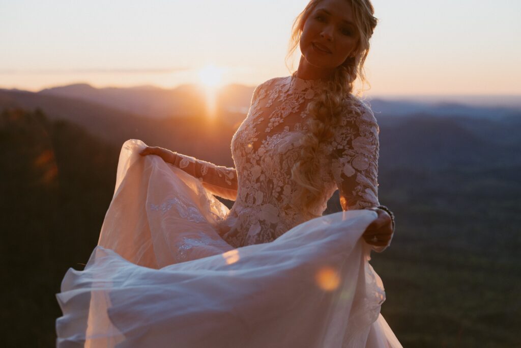 Woman in wedding dress spinning with mountains in the background at sunrise. 
