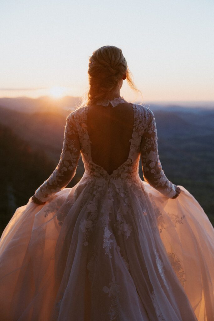 Woman in a wedding looking at sunrise over the mountains.