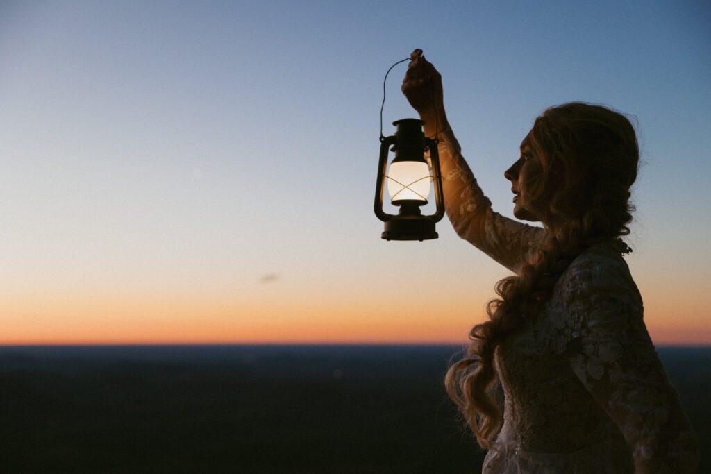 Woman holding a lantern and looking at mountains during sunrise. 