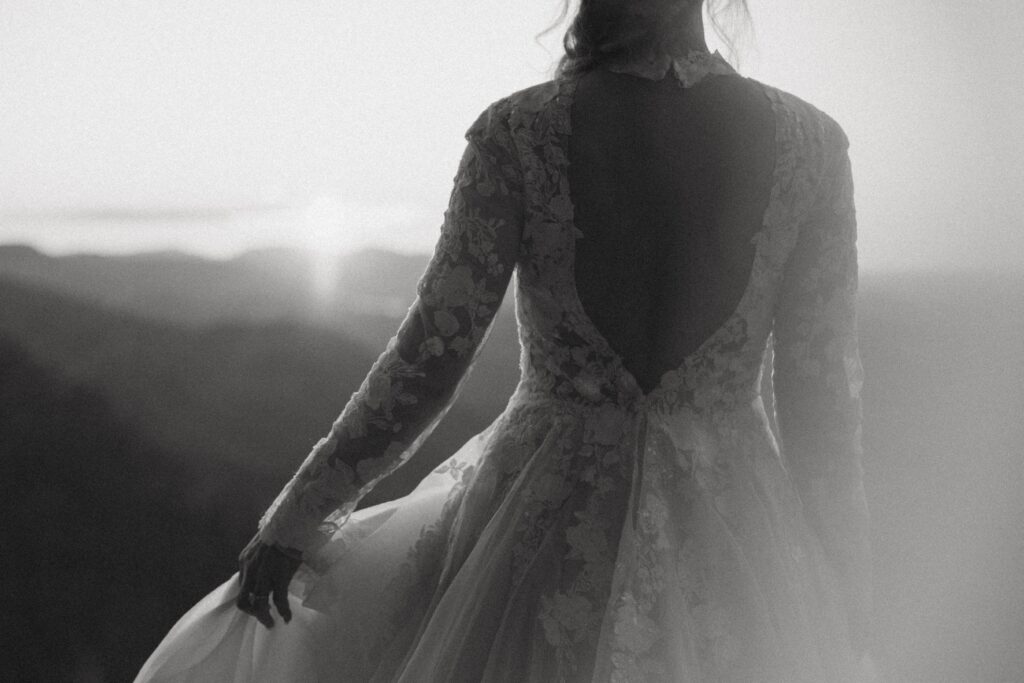 Woman in wedding dress holding the side with her left hand and looking at mountains.