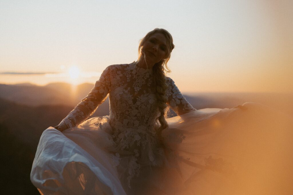 Woman in wedding dress spinning with mountains in the background at sunrise. 