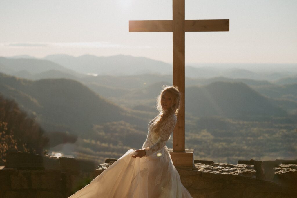 Woman in a wedding dress spinning in front of a cross with mountains in the background. 