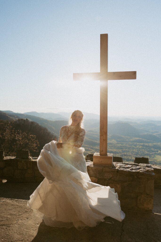 Woman in wedding dress spinning in front of cross with mountains in the background.