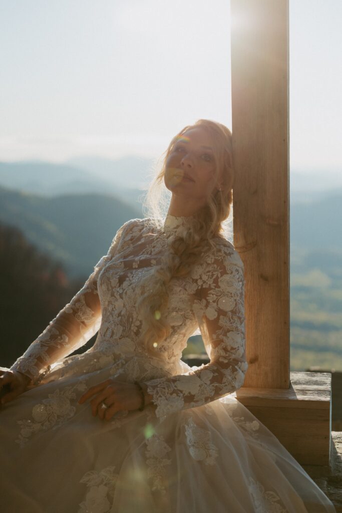 Woman in wedding dress leaning on a cross with mountains in the background.