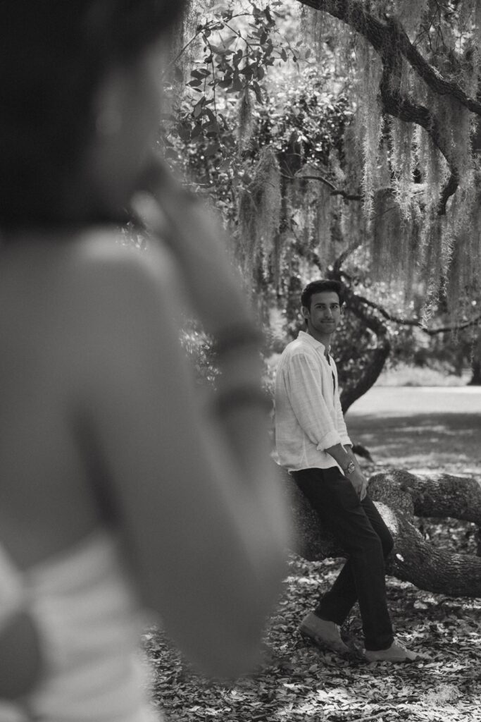 Man sitting on spanish moss tree limb looking at woman in foreground.