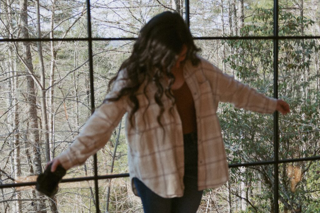 Woman with a camera standing in front of window with trees outside.