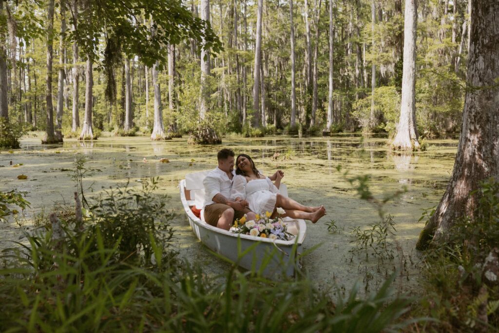 Couple sitting in boat at Cypress Gardens in South Carolina with flowers in front of the boat.