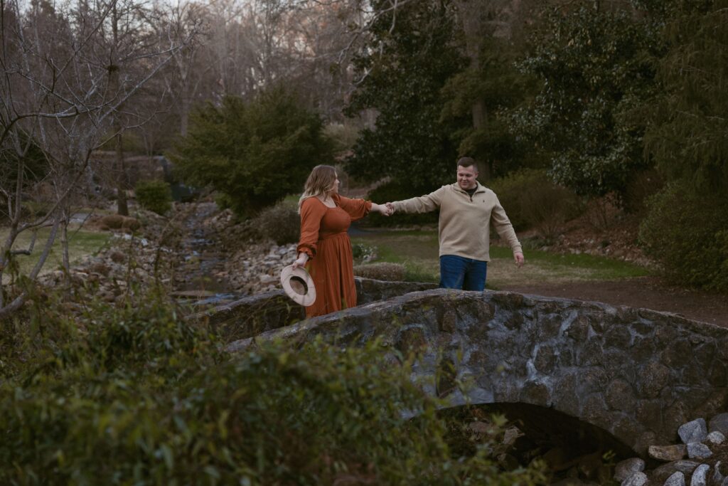 Couple holding hands on bridge at Rock Quarry Garden in Greenville, SC.