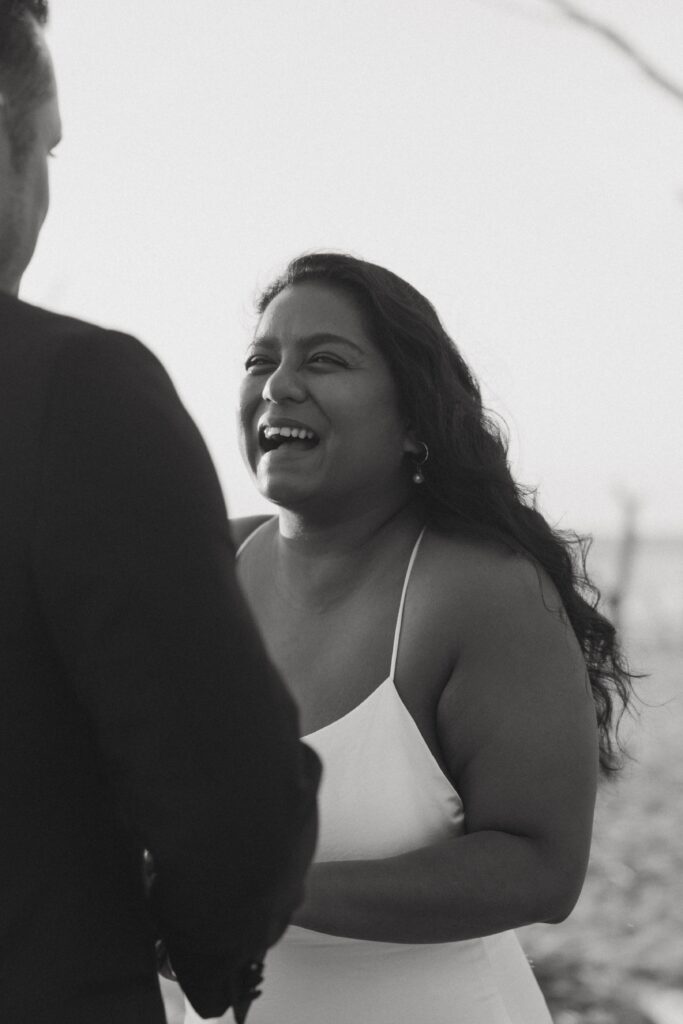 Woman in wedding dress laughing while looking at man.