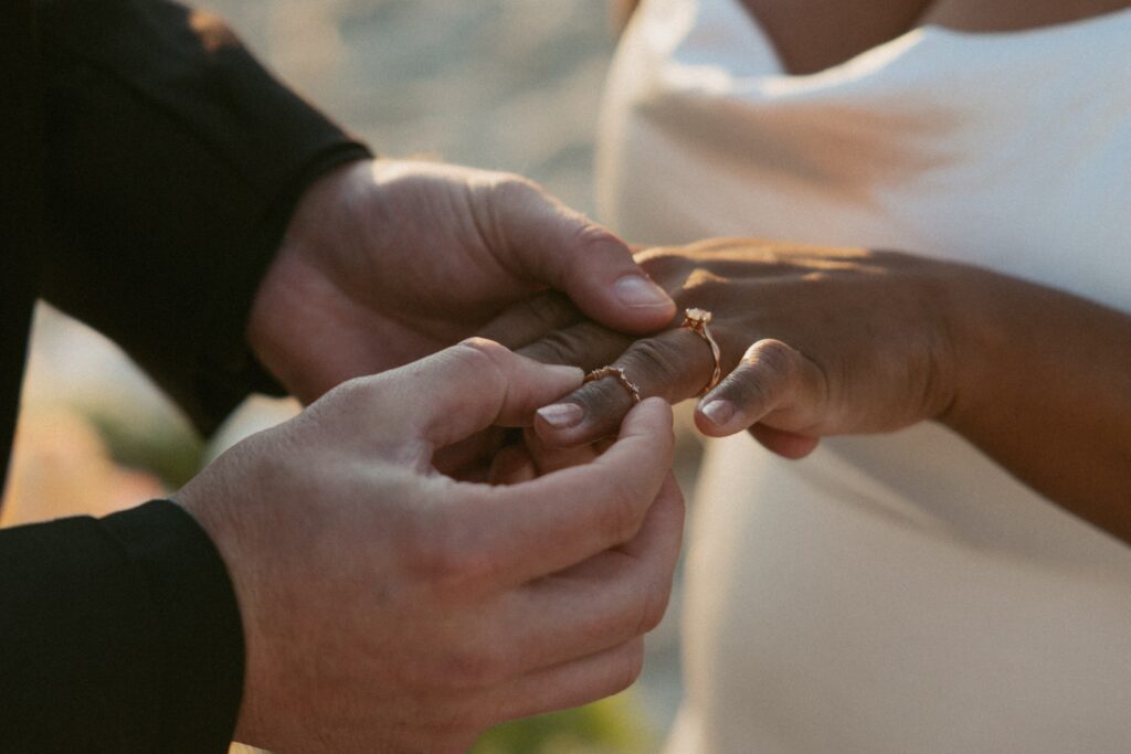 Close up photo of man putting wedding ring on woman's hand.