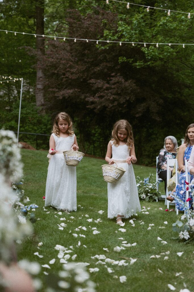 Two girls in dresses walking down wedding aisle and dropping flower pedals.