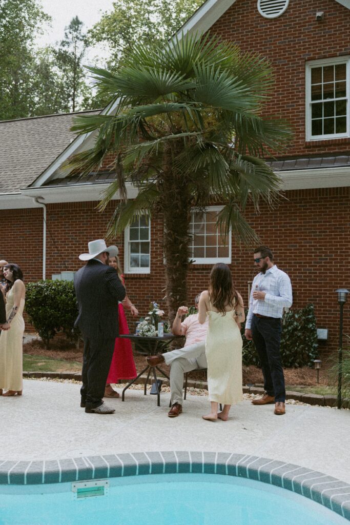 Group of people standing at table with a palm tree behind them and pool in front of them.