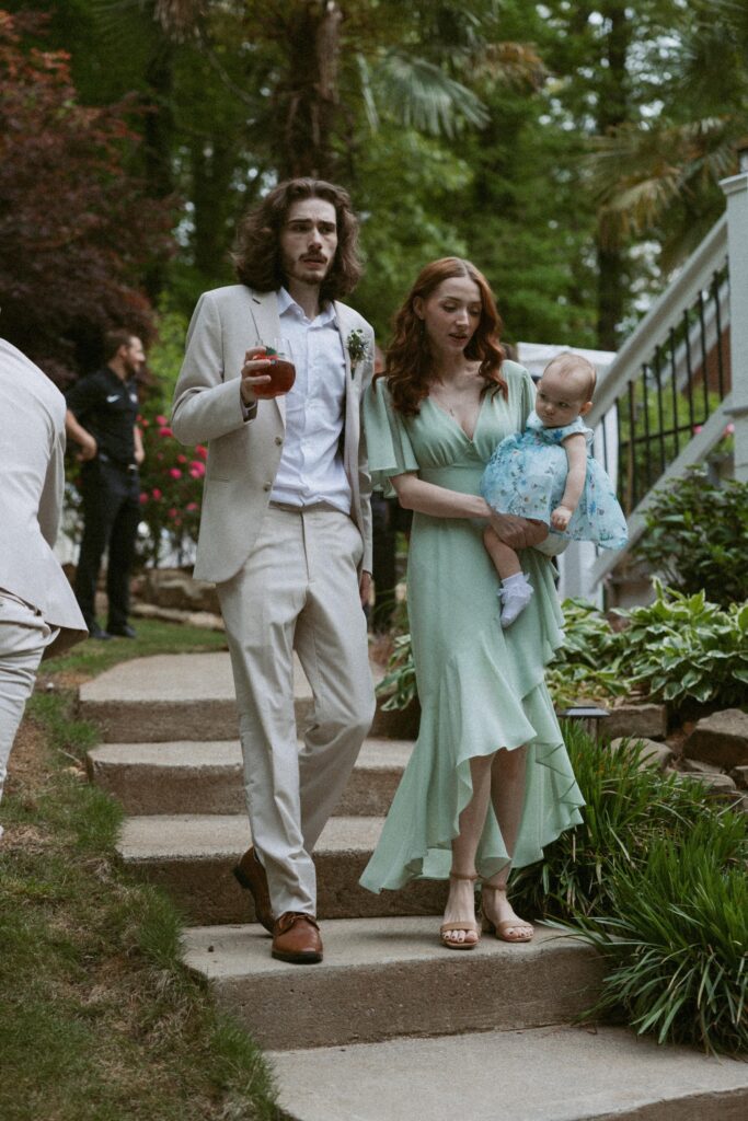 Man and woman holding a baby while walking down stairs at a backyard wedding.