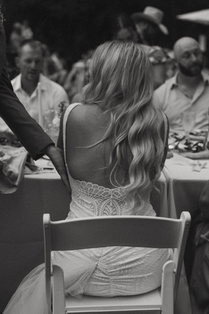 Woman sitting in chair in wedding dress looking at someone beside her.