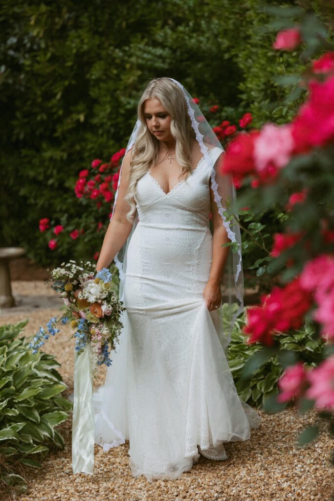 Woman in wedding dress walking down a garden path with pink roses around her.