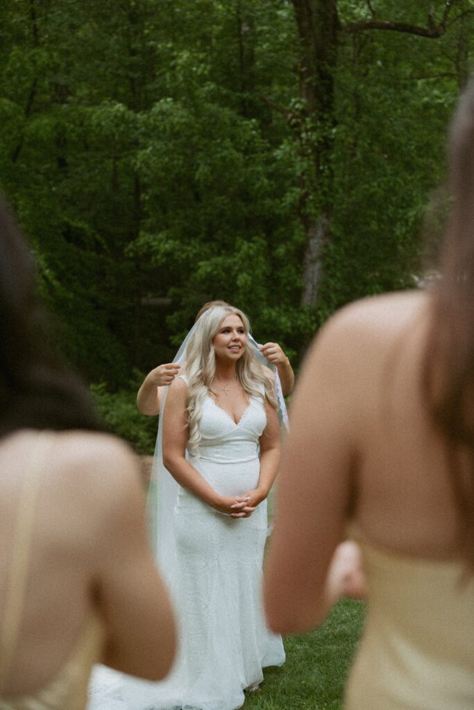 Two girls in foreground looking at woman in wedding dress getting her veil fixed.