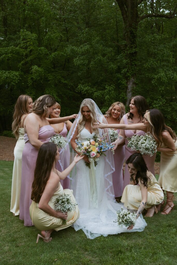 Woman in wedding dress standing with bridesmaids while they fix her dress.