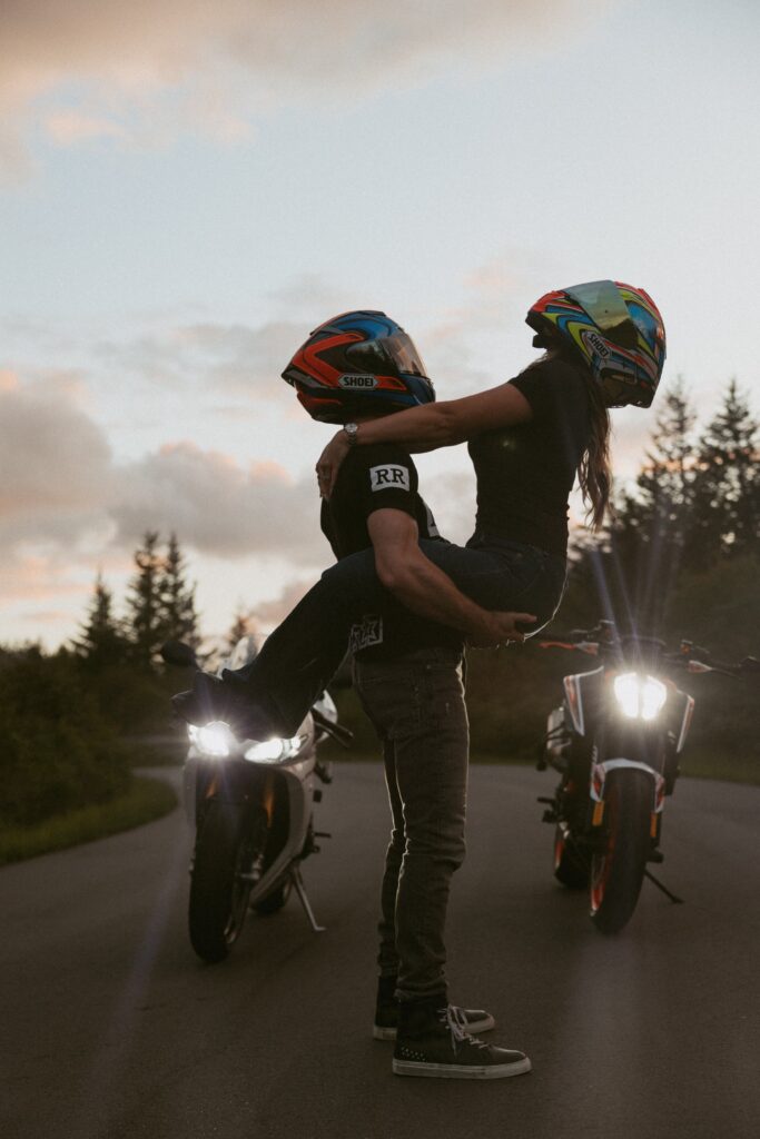 Man holding woman in front of motorcycles with helmets on. 