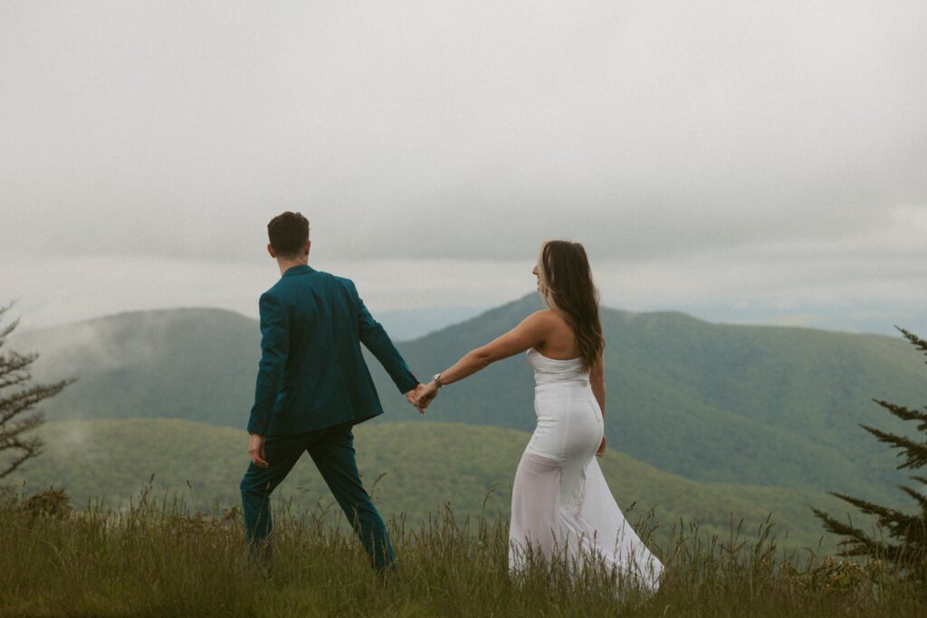 Man and woman holding hands and walking with mountains in background.