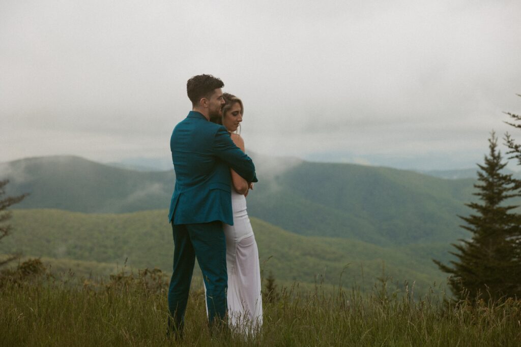 Man and woman hugging each other while looking out at mountains.