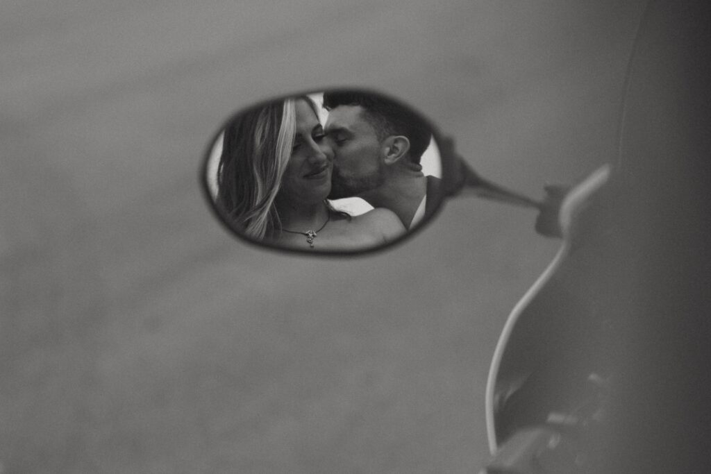 Man kissing woman on the cheek in a motorcycle mirror.