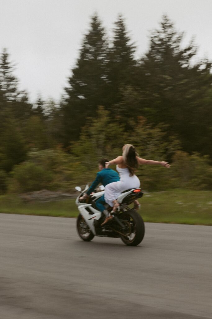 Man and woman riding a motorcycle with womans hands wide open.