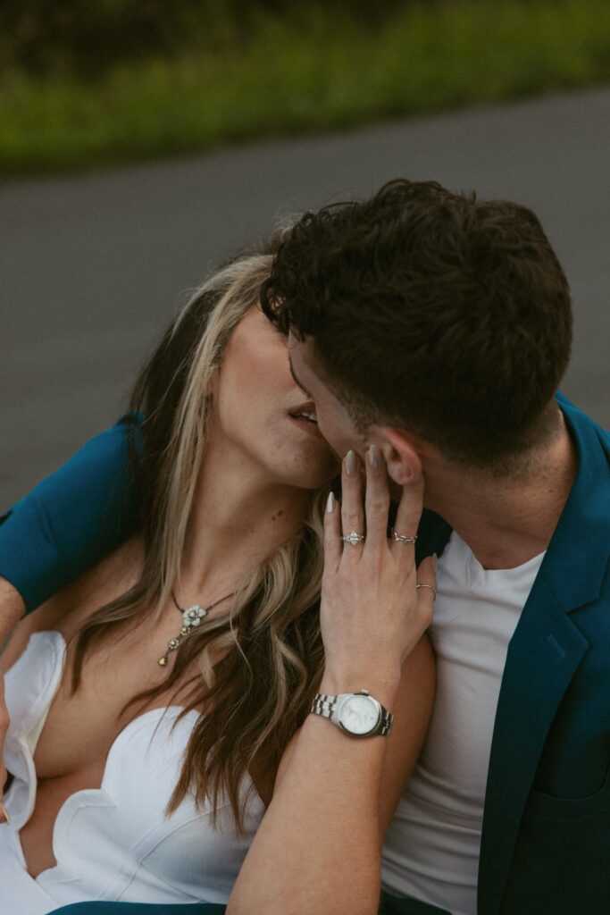 Woman holding mans face and pulling him in for a kiss while they sit in the road.