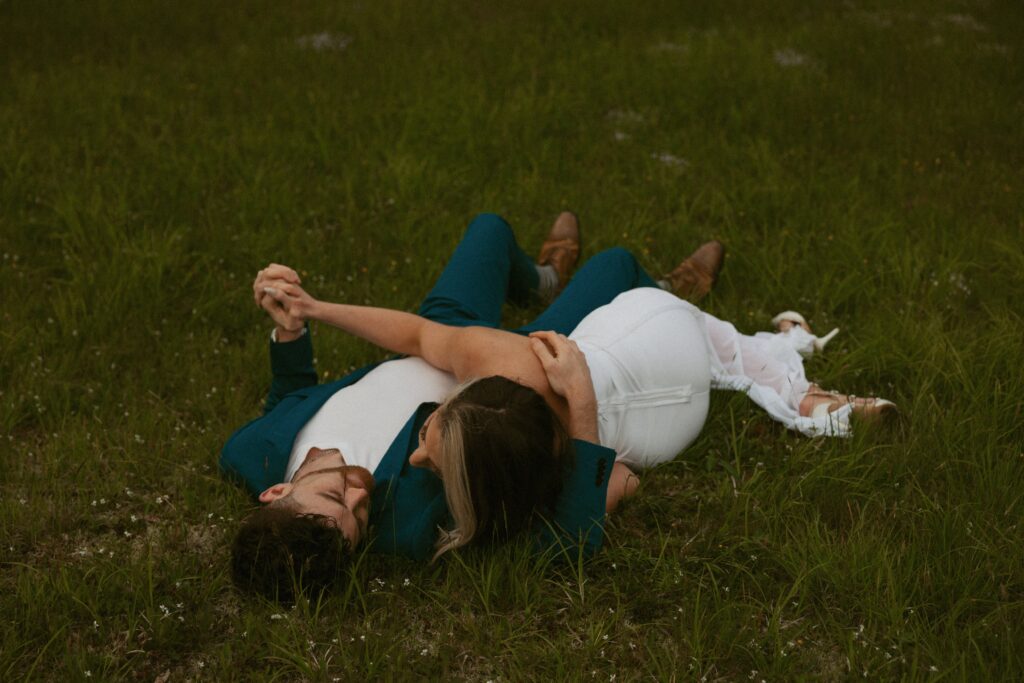 Man and woman holding hands and laying in grass with flowers.