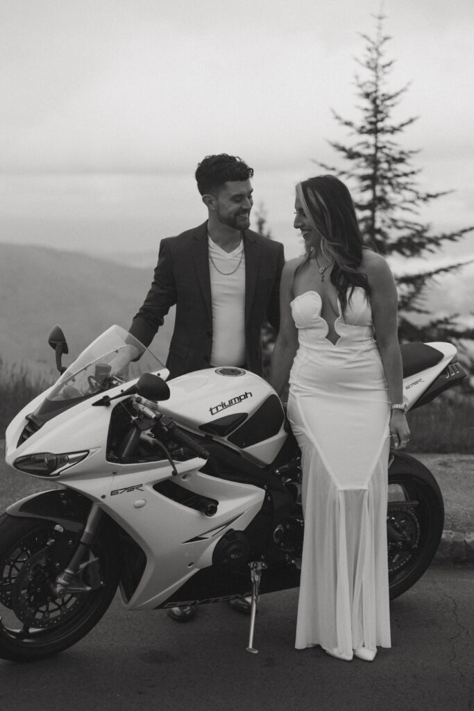 Man and woman smiling at each other and leaning on motorcycle.