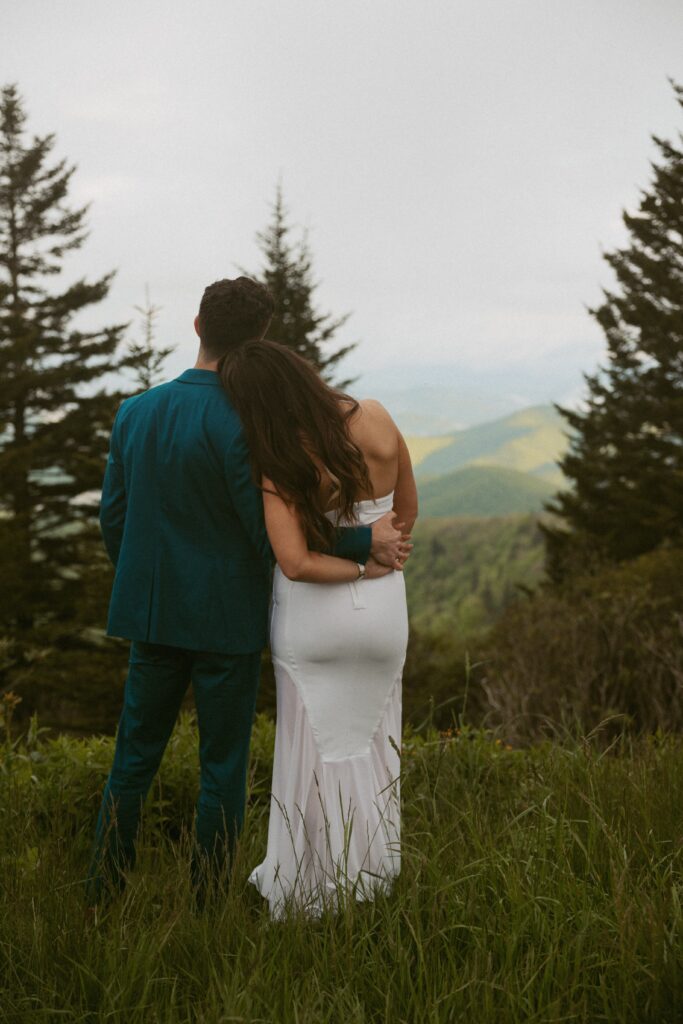 Man and woman hugging and holding hands looking at mountains.