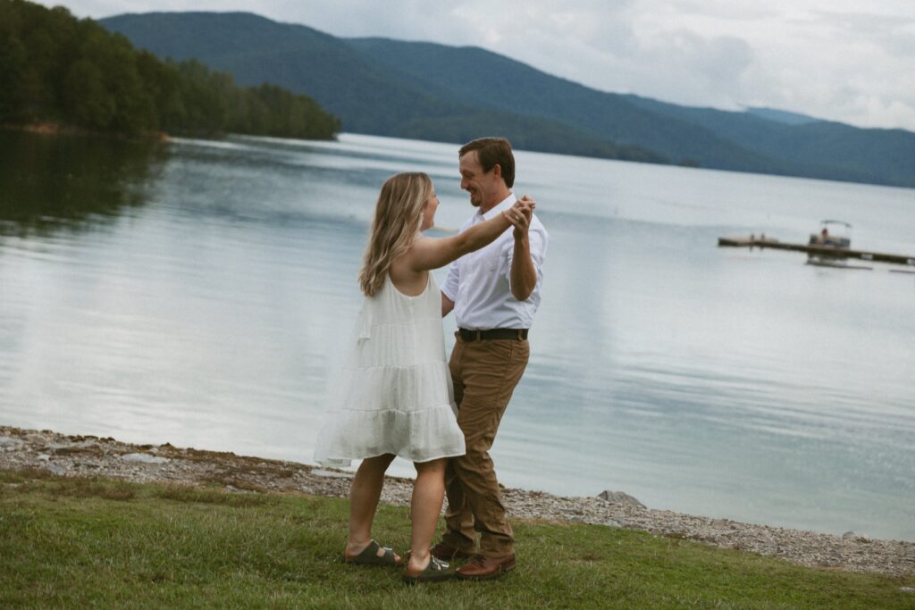 Man and woman dancing and laughing with the mountains and lake behind them. 