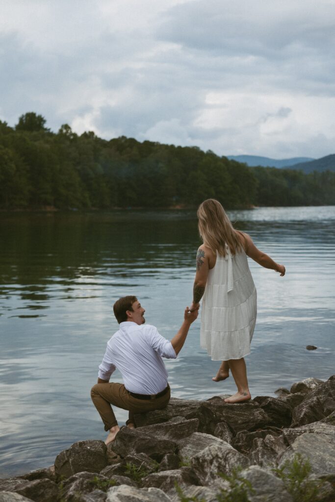 Man sitting on the rocks helping a woman walk towards him. 