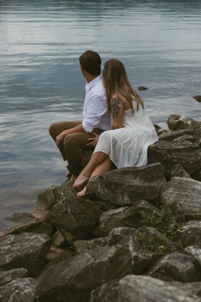 Woman sitting behind a man on the rocks looking at the lake. 