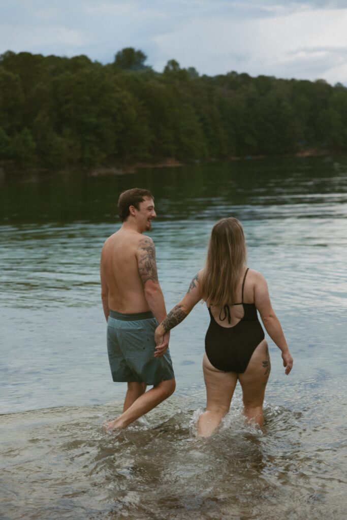 Man and woman holding hands while walking into the water.