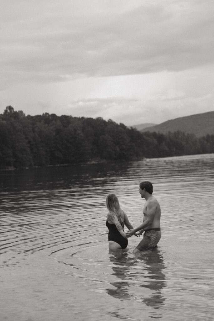 Woman holding a mans hands and leading him while they walk through the water. 