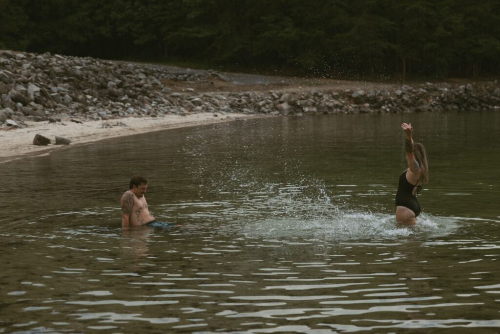 Woman standing up in the water and splashing a man that is sitting in the water.