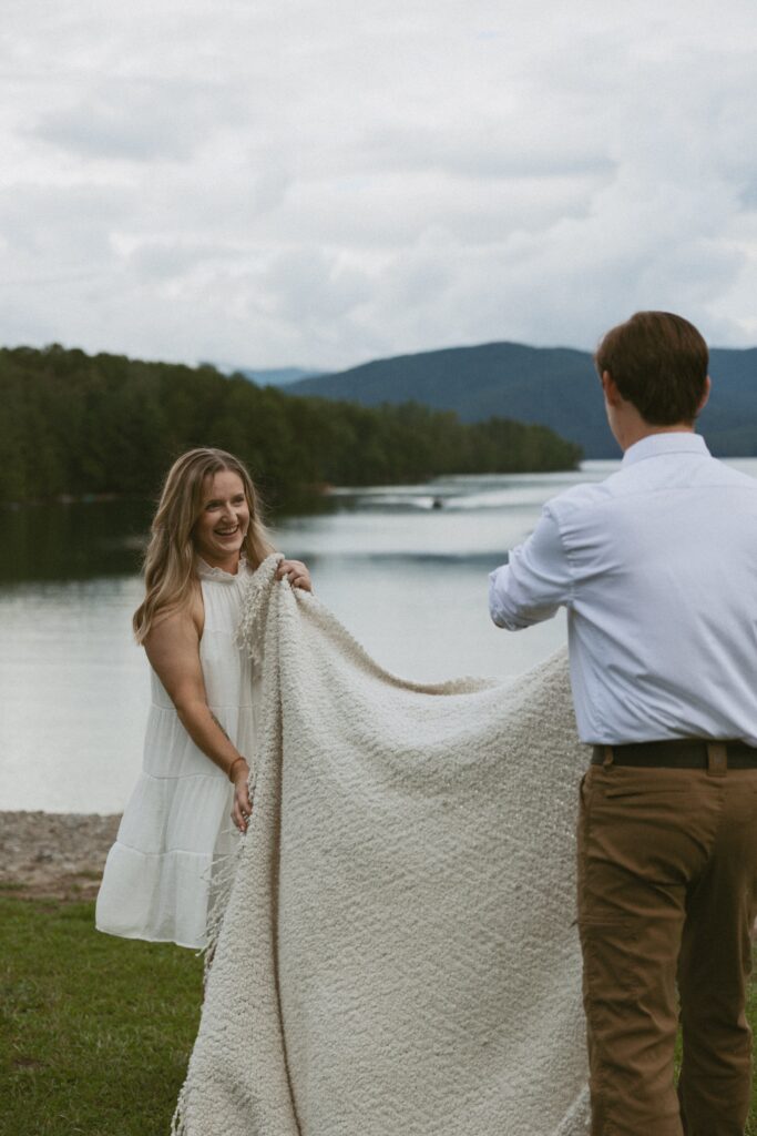 Woman smiling at a man while they lay a blanket down in the grass.