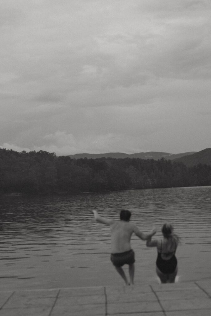 Man and woman jumping off of a dock into the lake.