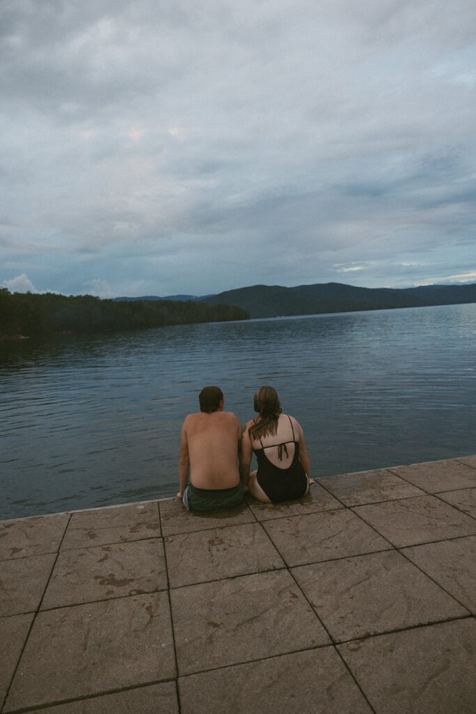 Man and woman sitting on a dock looking at the lake and mountains.