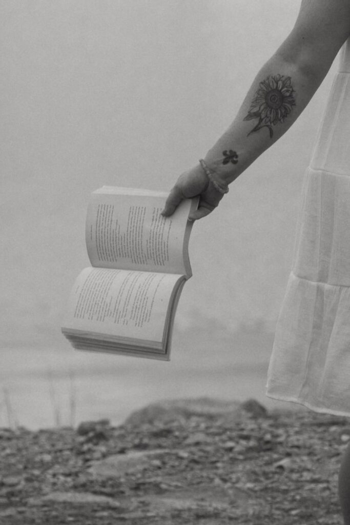 Close up of a woman with tattoos holding a book open.